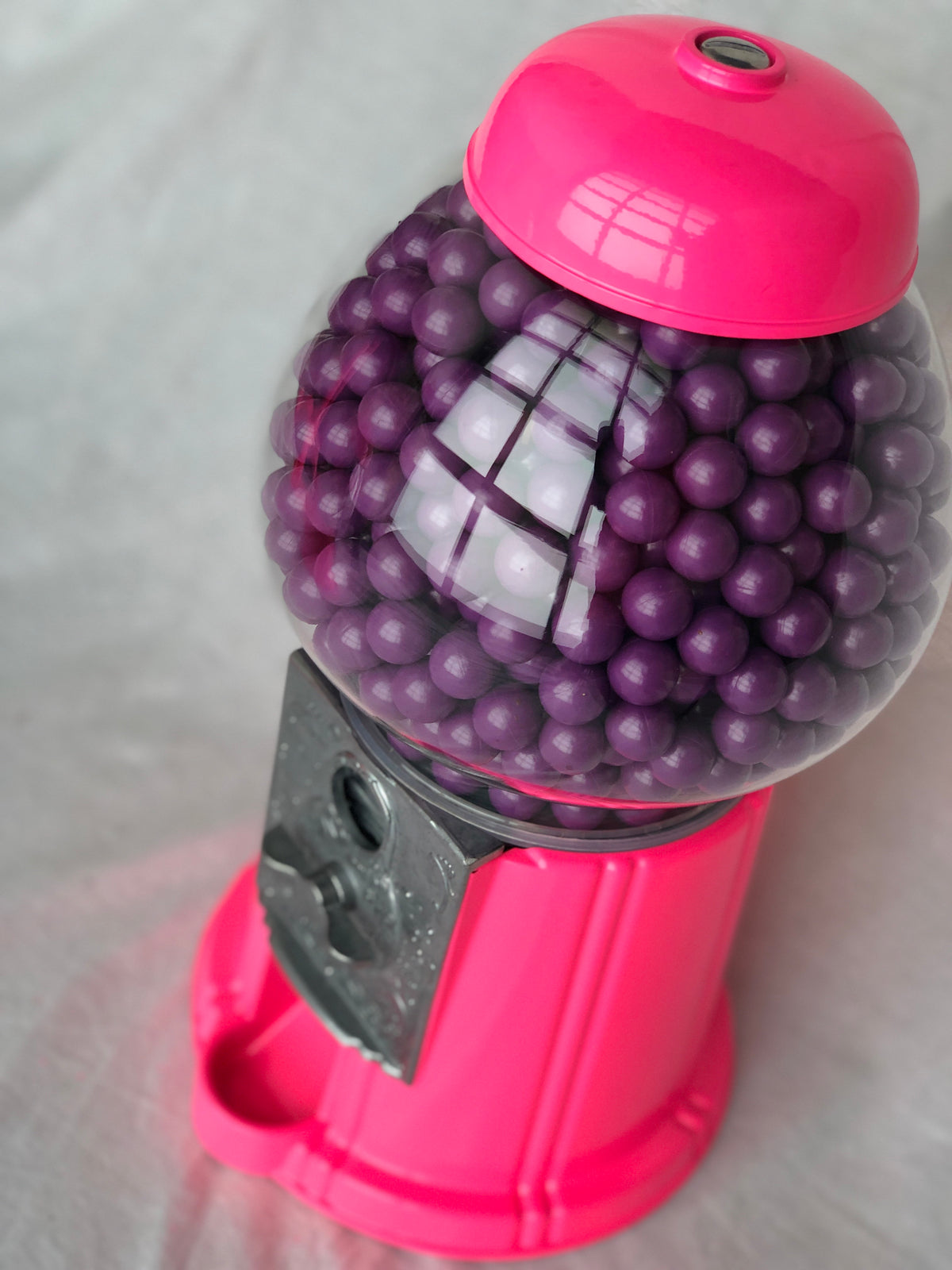 Pink gumball machine filled with purple gumballs on a light gray background