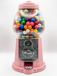 A pink gumball machine filled with multicolored gumballs, featuring a real glass globe and a metal base.